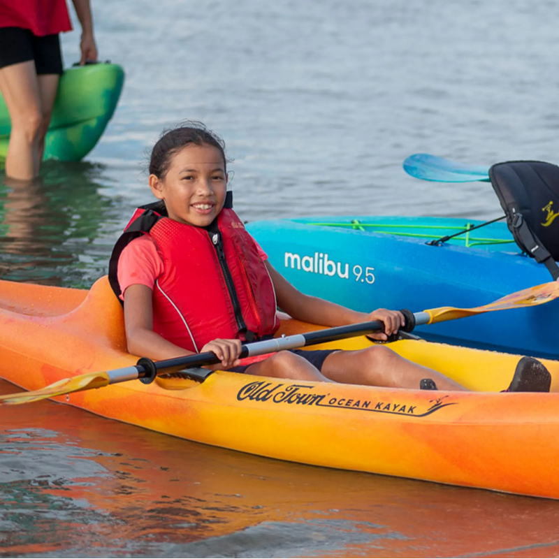 A child wearing Old Town Inlet Jr Kids' Foam Life Jacket – Red and riding a kayak