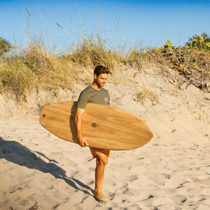 A man carrying a Surfboard Trading Co. Summer Wind Paulownia EPS Surfboard