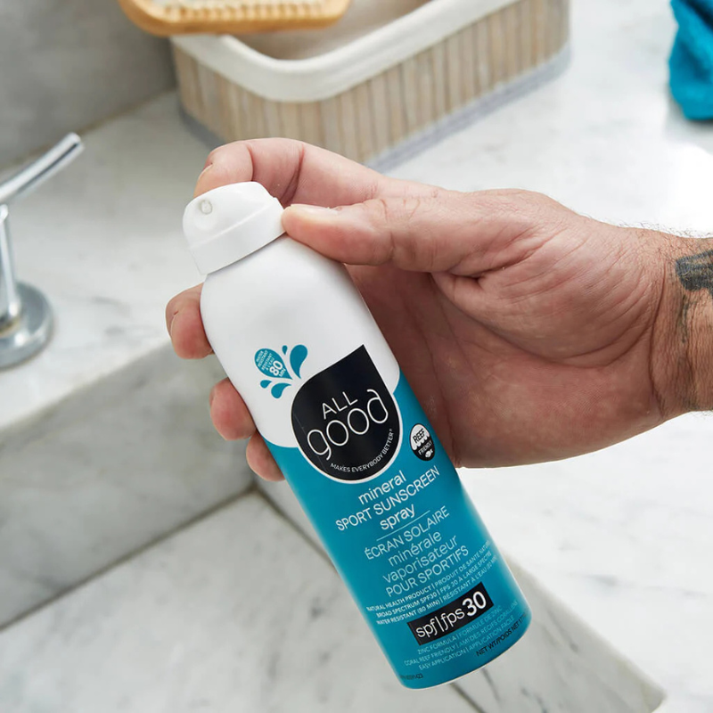 A man holding All Good SPF30 Sport 6 oz Mineral Sunscreen Spray