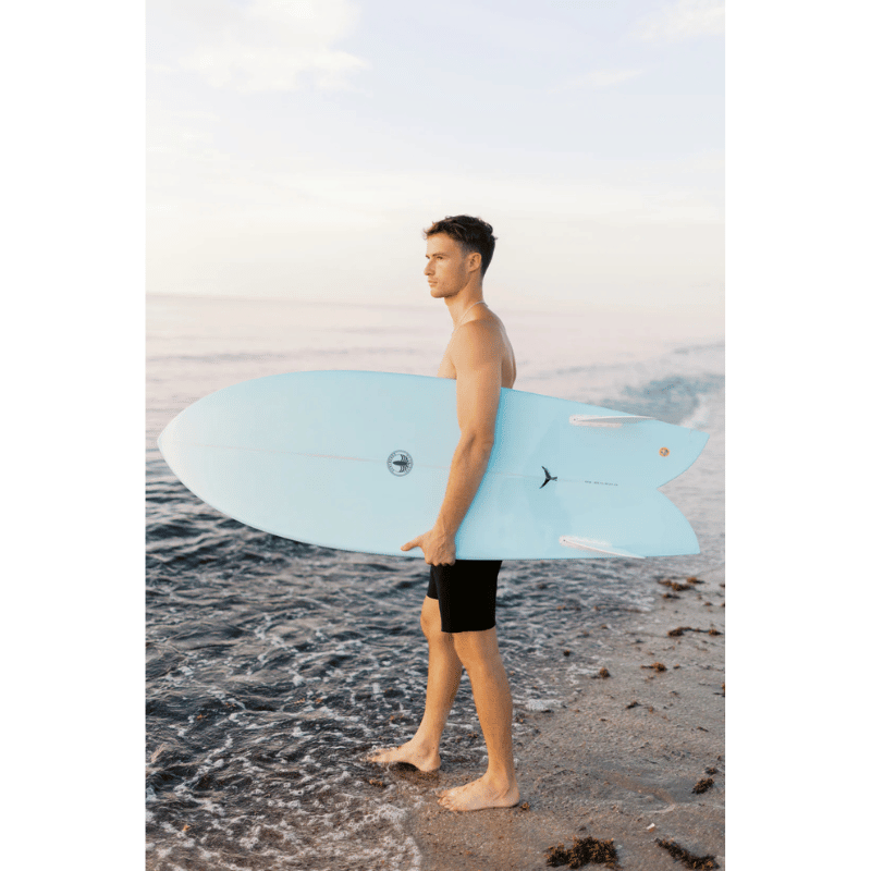 A surfer carrying a Surfboard Trading Co. Finlet Twin Fish EPS Surfboard - Cutlap Aqua