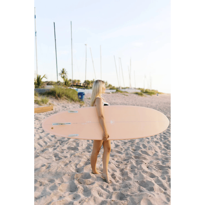 An intermediate surfer carrying a Surfboard Trading Co. ANY DAY Mid Length EPS Surfboard – Peach 