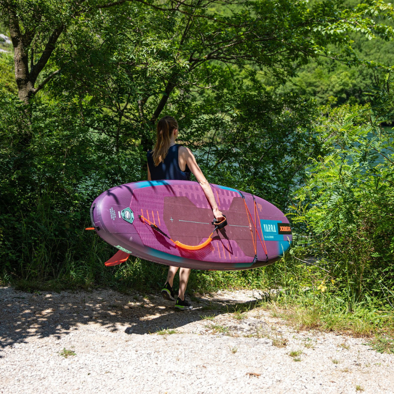 An woman carrying a Jobe Aero Yarra 10’6” Inflatable Purple Paddle Board iSUP