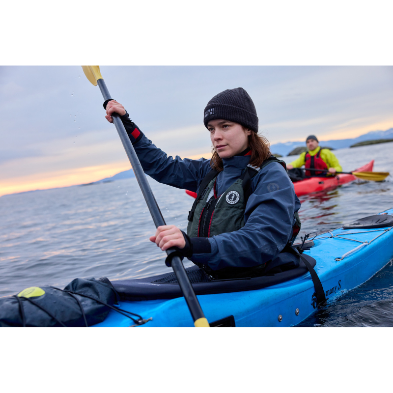 An woman wearing Mustang Survival L/XL Rebel Women's Foam Life Jacket - Grey and riding a kayak