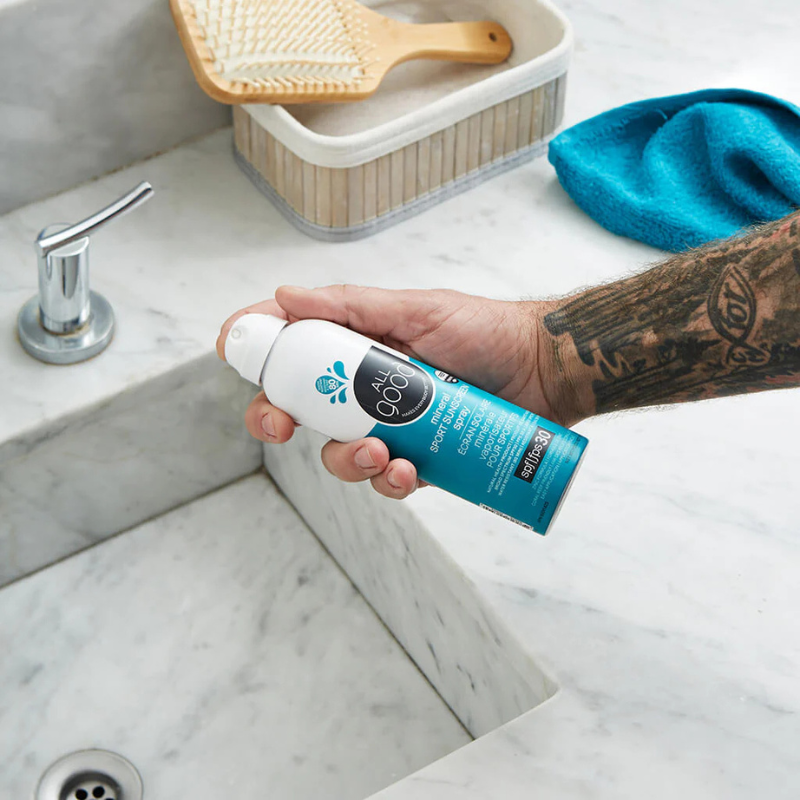 A person showing All Good SPF30 Sport 6 oz Mineral Sunscreen Spray