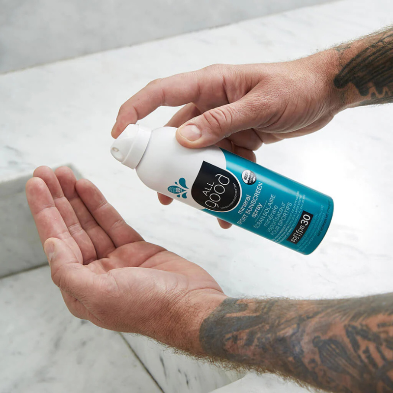 A person using All Good SPF30 Sport 6 oz Mineral Sunscreen Spray