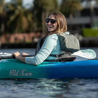 Thumbnail for A person wearing Old Town Solitude II Women’s Foam Life Jacket – Silver and riding a kayak