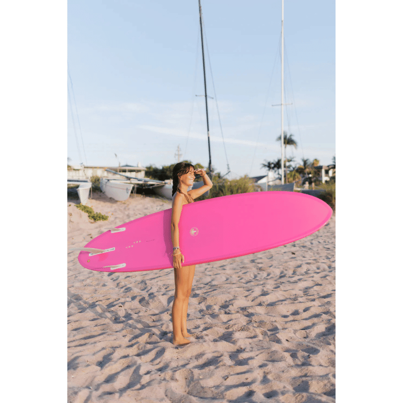 Lifestyle photo of a person carrying a Surfboard Trading Co. ANY DAY Mid Length EPS Surfboard – Hot Pink