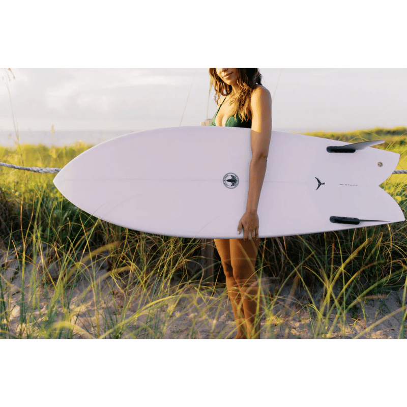 A surfer carrying a Surfboard Trading Co. Finlet Twin Fish EPS Surfboard – Lilac