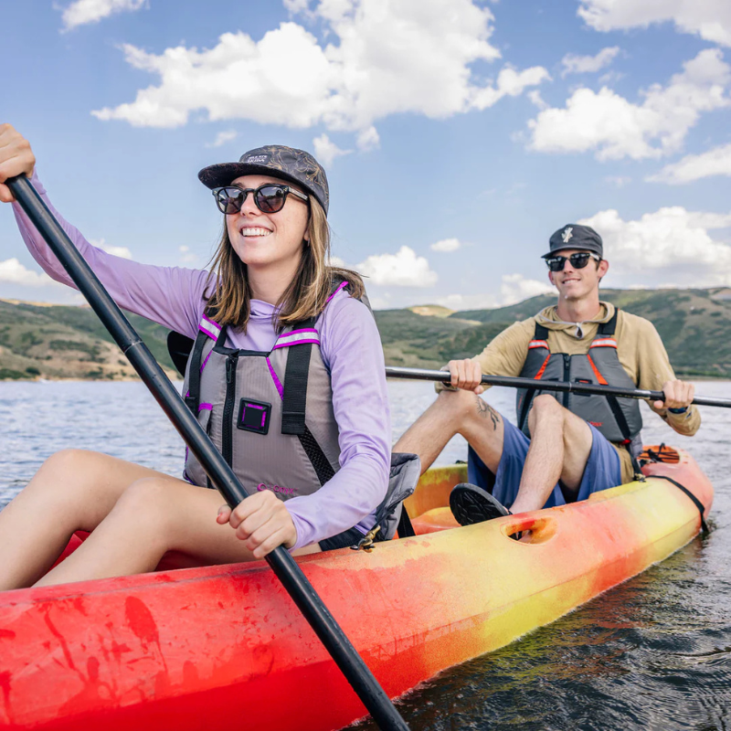 Two people riding a kayak wearing Onyx MoveVent Dynamic Foam Life Jackets